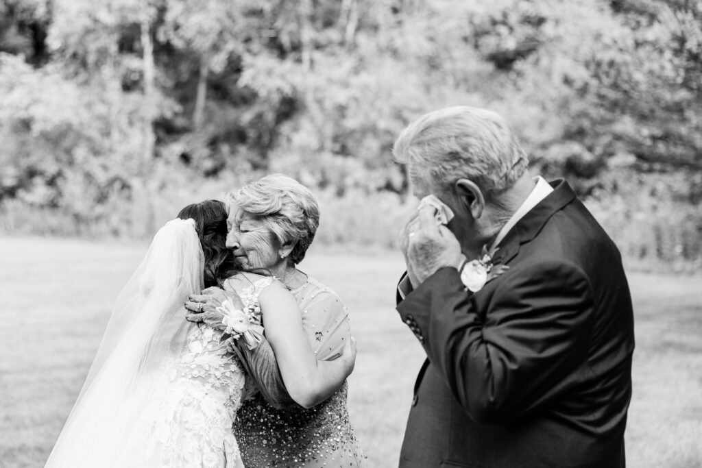A bride hugs her tearful Grandmother while her Grandfather is drying his eyes with a tissue in the background